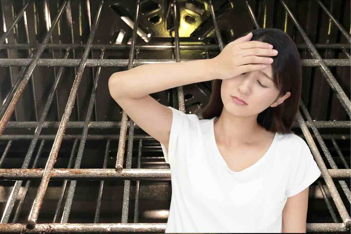 Donna con mano sul viso, dietro di lei griglie forno