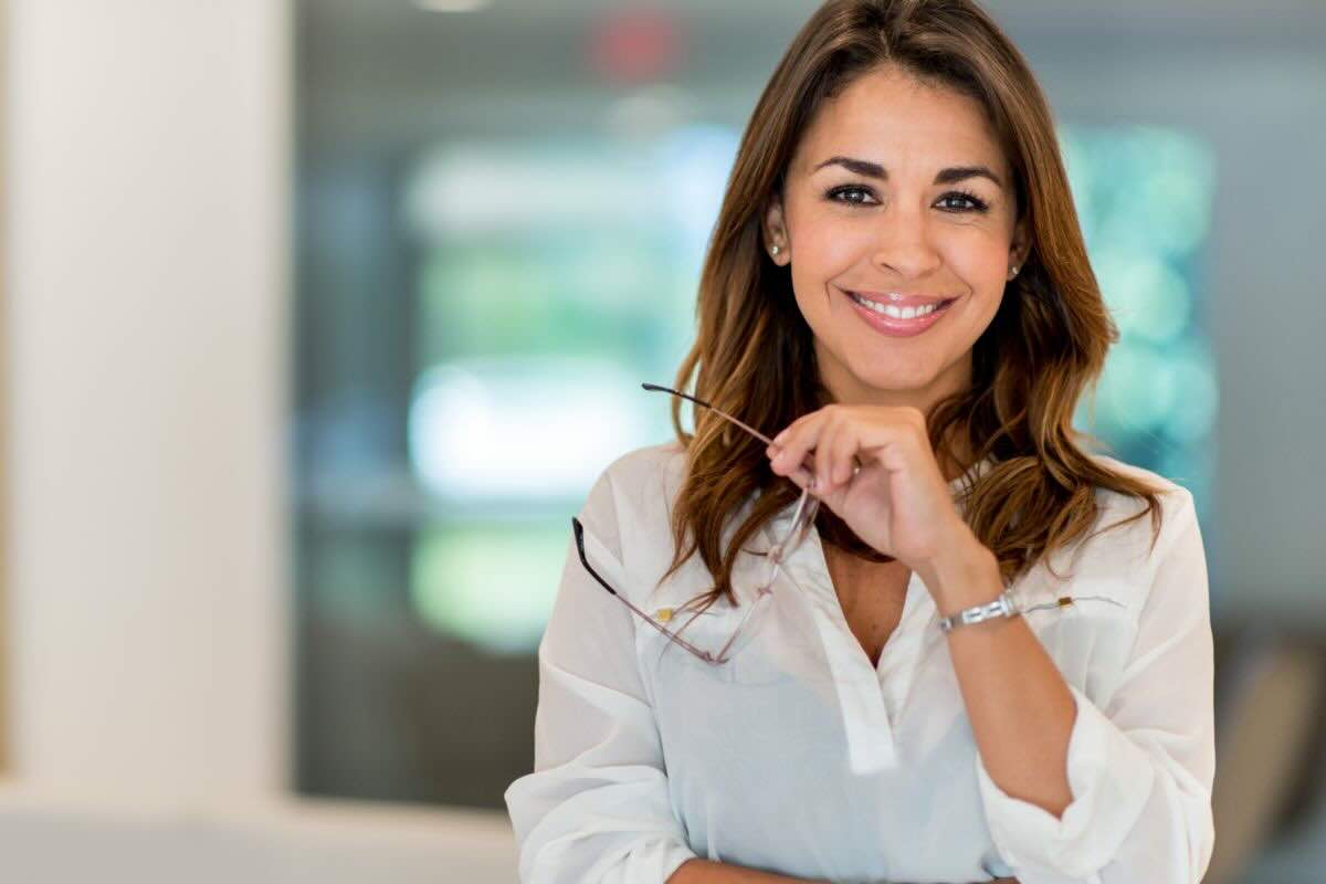 Donna con camicia bianca, occhiali da vista in mano, sorridente