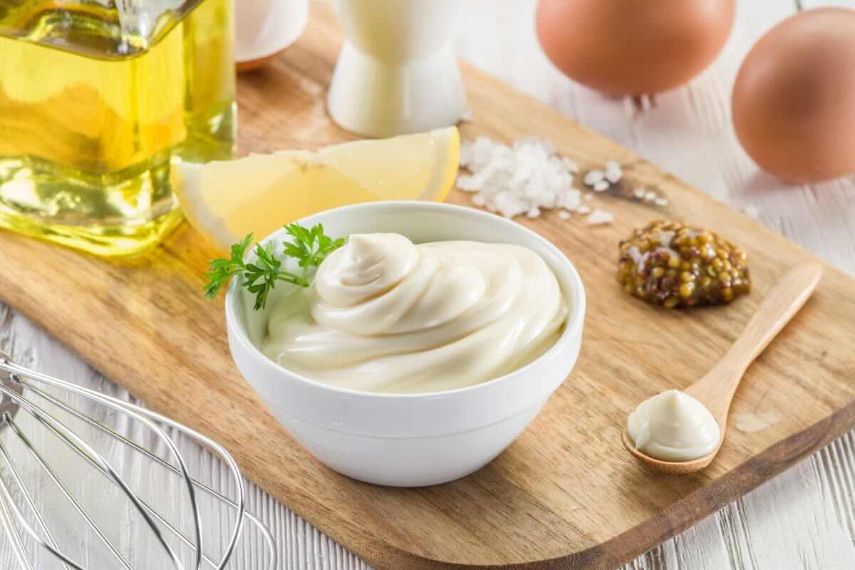 Maionese in ciotola, ingredienti vari sul tagliere come limone, sale