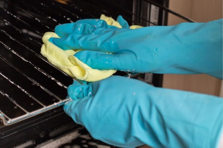 Mani con guanti azzurri e panno giallo puliscono griglie del forno
